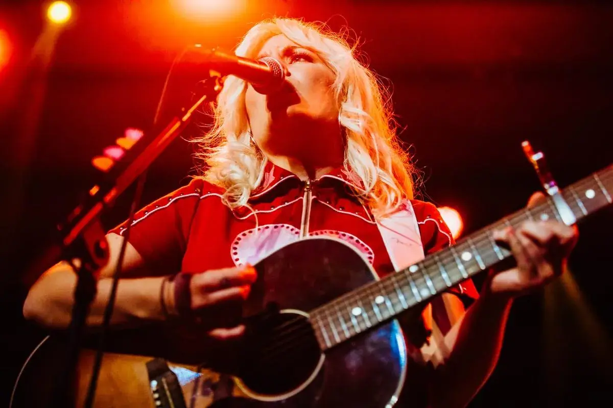 Maja Francis sjunger och spelar gitarr på en scen, upplyst av rött ljus.