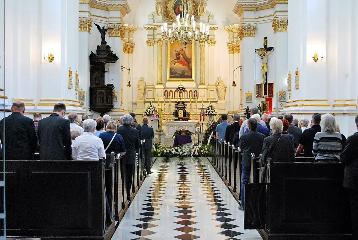 Uroczystość pogrzebowa w kościele. Ludzie stoją w ławkach, żegnając zmarłego teścia.