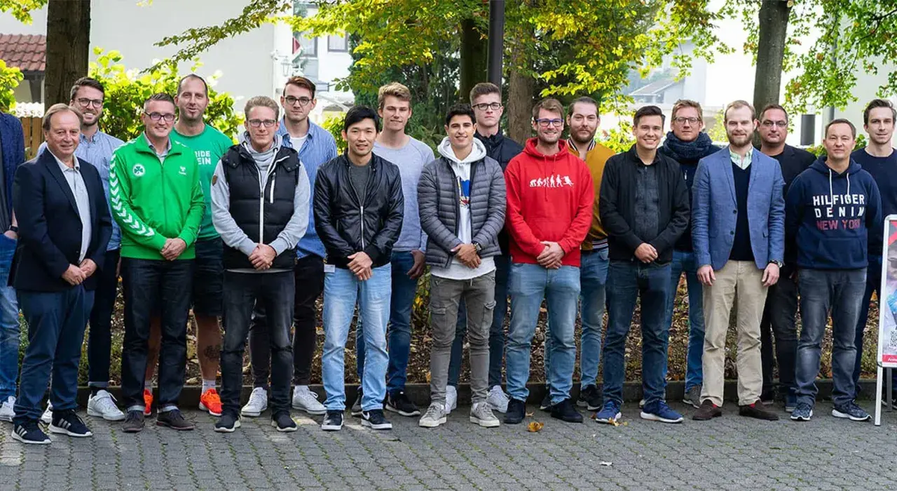 Eine Gruppe junger Männer steht lächelnd im Freien. Vielleicht sind sie angehende Fußball-Scouts, die ihre Ausbildung beginnen.