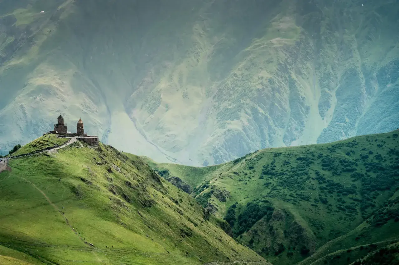 Kościół na wzgórzu w gruzińskich górach, otoczony zielonymi zboczami i majestatycznymi szczytami.