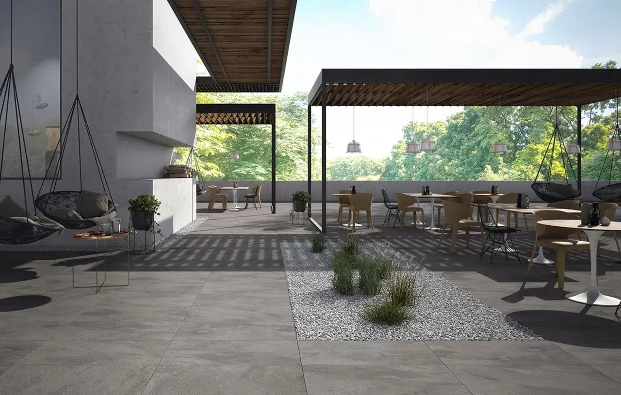Spazio esterno moderno con tavoli, sedie e altalene, pavimentato con eleganti mattonelle per esterni grigie.