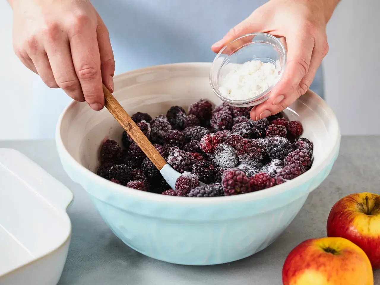 Hände mischen Brombeeren mit Zucker für schnelle und einfache Brombeeren Rezepte. Äpfel liegen daneben.