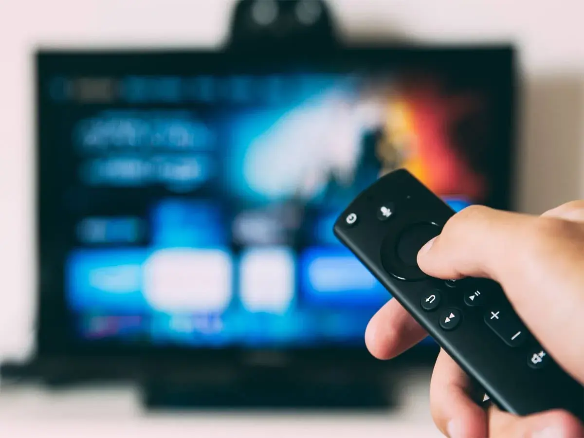 Fernsehen ohne Anschluss und ohne Internet: Eine Hand hält eine Fernbedienung vor einem unscharfen Bildschirm mit bunten Menüs.