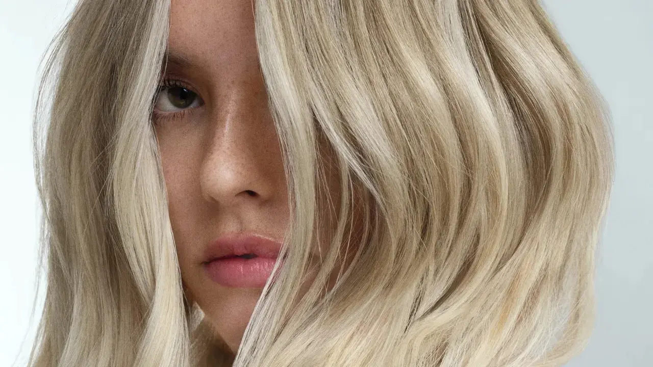 Primer plano de una mujer con pelo rubio matizado, con mechones cayendo sobre su rostro.