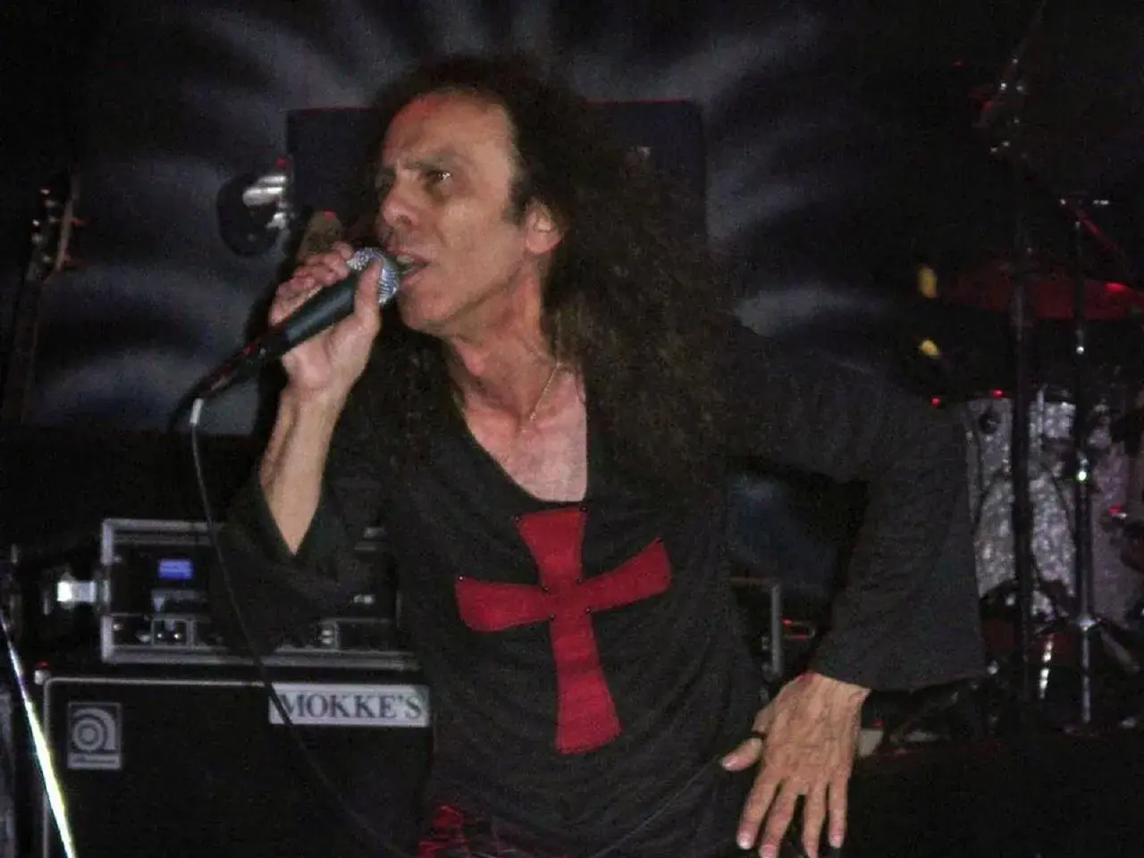 Ronnie James Dio zespół śpiewa do mikrofonu, ubrany w czarną koszulkę z czerwonym krzyżem.