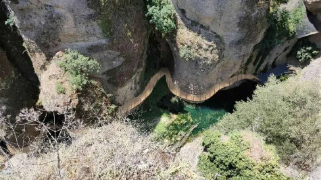 Un puente serpentea sobre el agua verde en el tajo de Ronda, rodeado de rocas y vegetación.