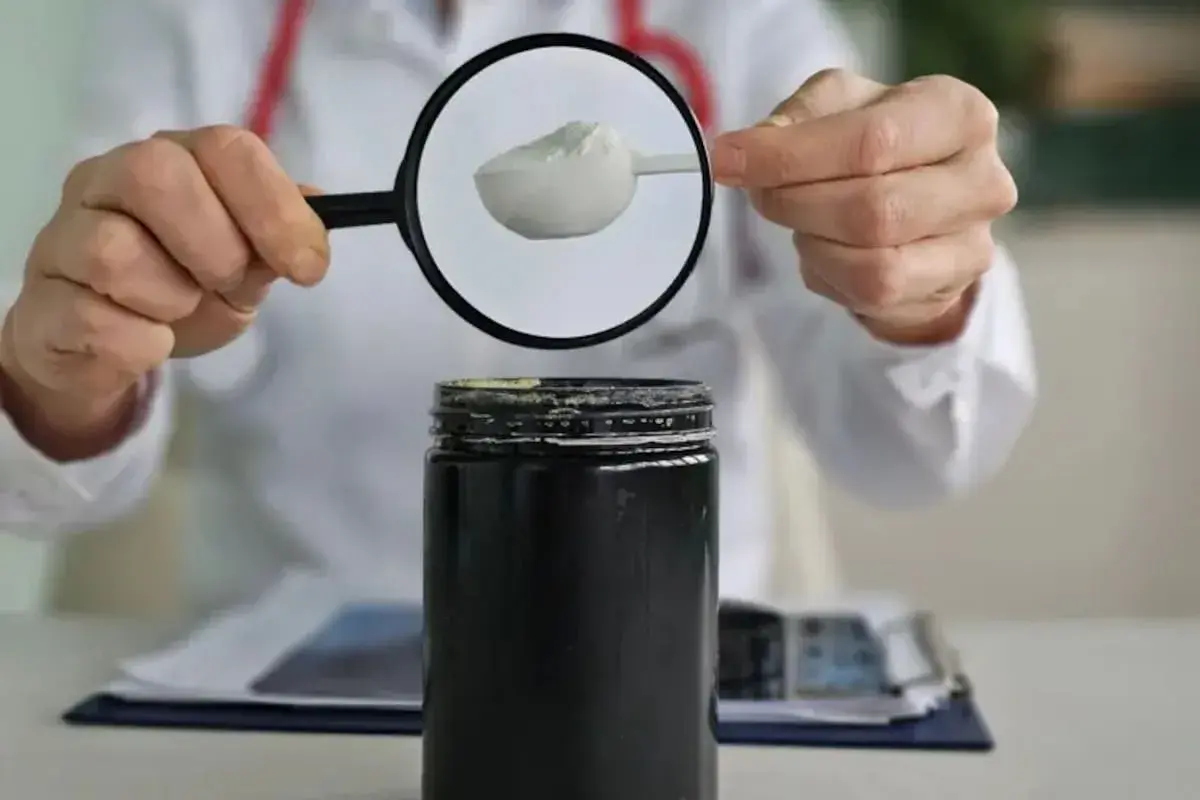 Persona con bata blanca examina con lupa polvo blanco de un envase, investigando creatina efectos secundarios.