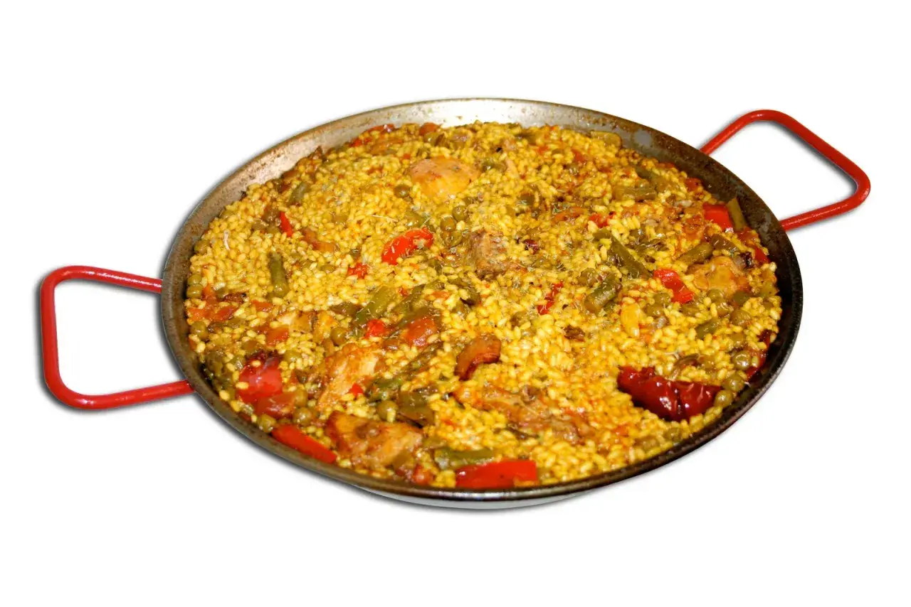 En stor paella med ris, kyckling, gröna bönor och paprika i en traditionell paellapanna med röda handtag.