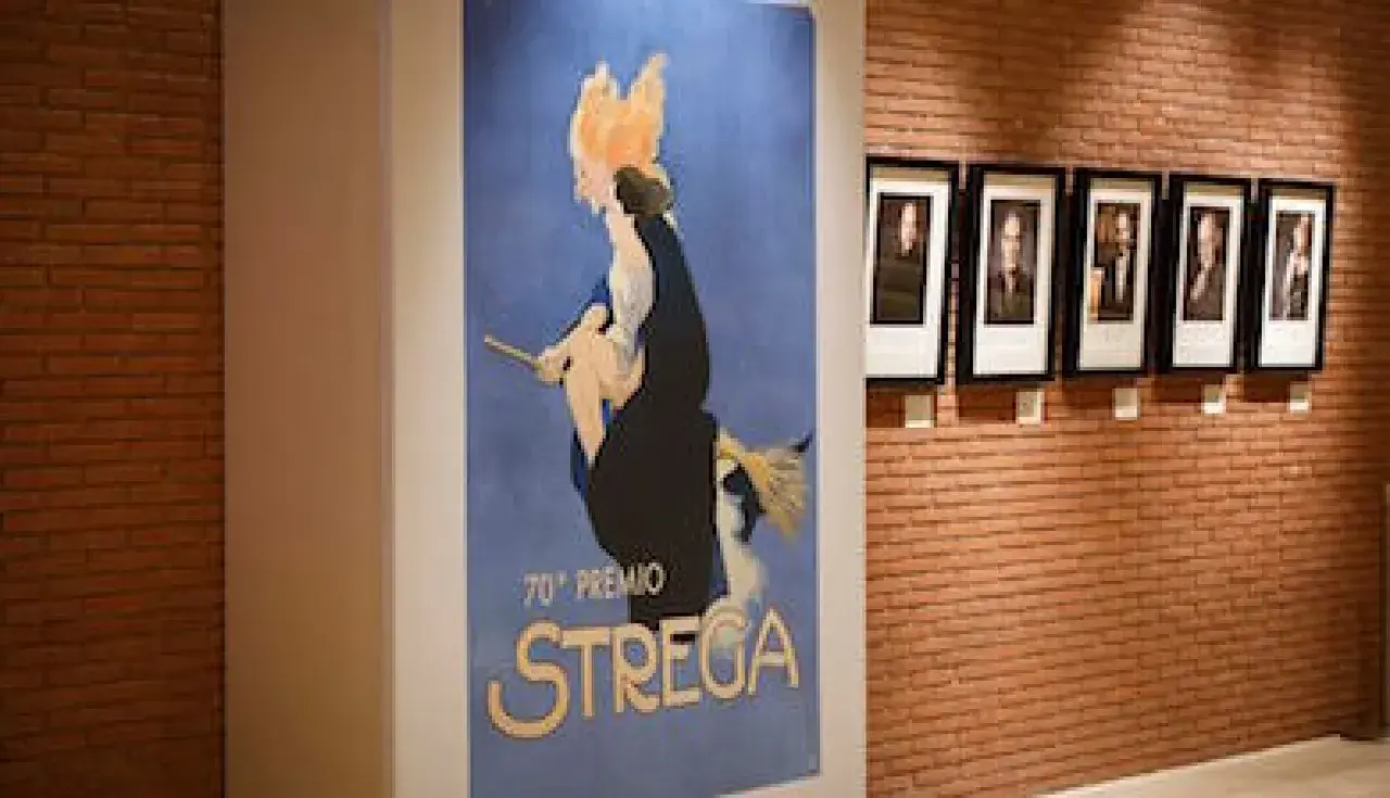 Un poster vintage celebra il 70° Premio Strega, con ritratti di autori appesi su una parete di mattoni.