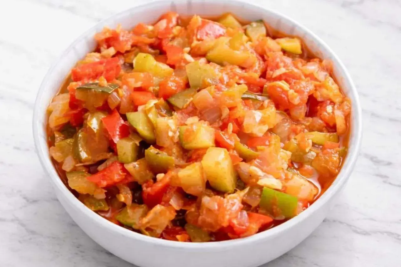 Un tazón blanco lleno de pisto manchego, un guiso vibrante de verduras picadas como tomate, pimiento y calabacín.