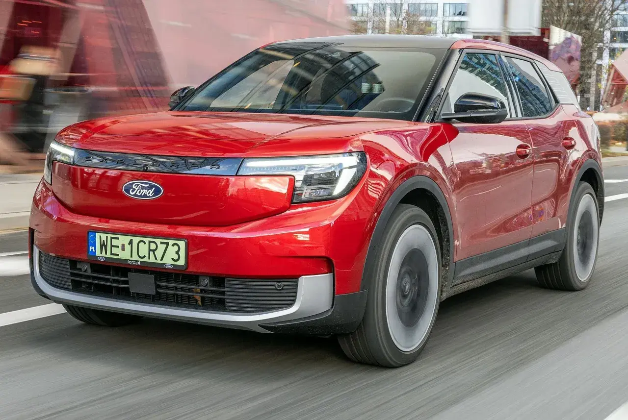 Czerwony Ford Explorer, nowoczesny SUV, pędzi po drodze, odbijając miejski krajobraz w swojej lśniącej karoserii.