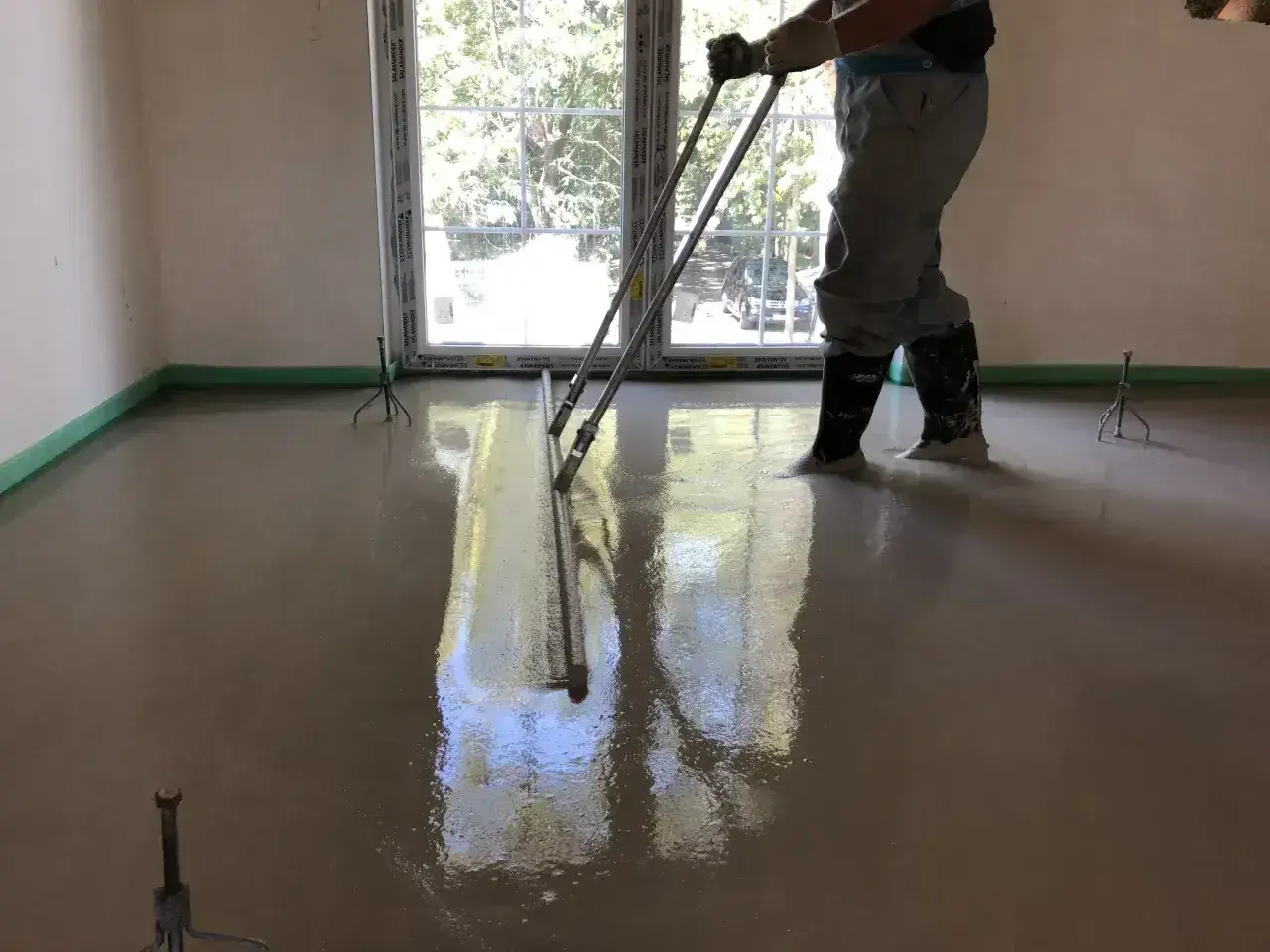 Pracownik wylewa beton, wyrównując go łaty. To kluczowe dla obliczenia, ile potrzeba cementu na 1m2 wylewki.