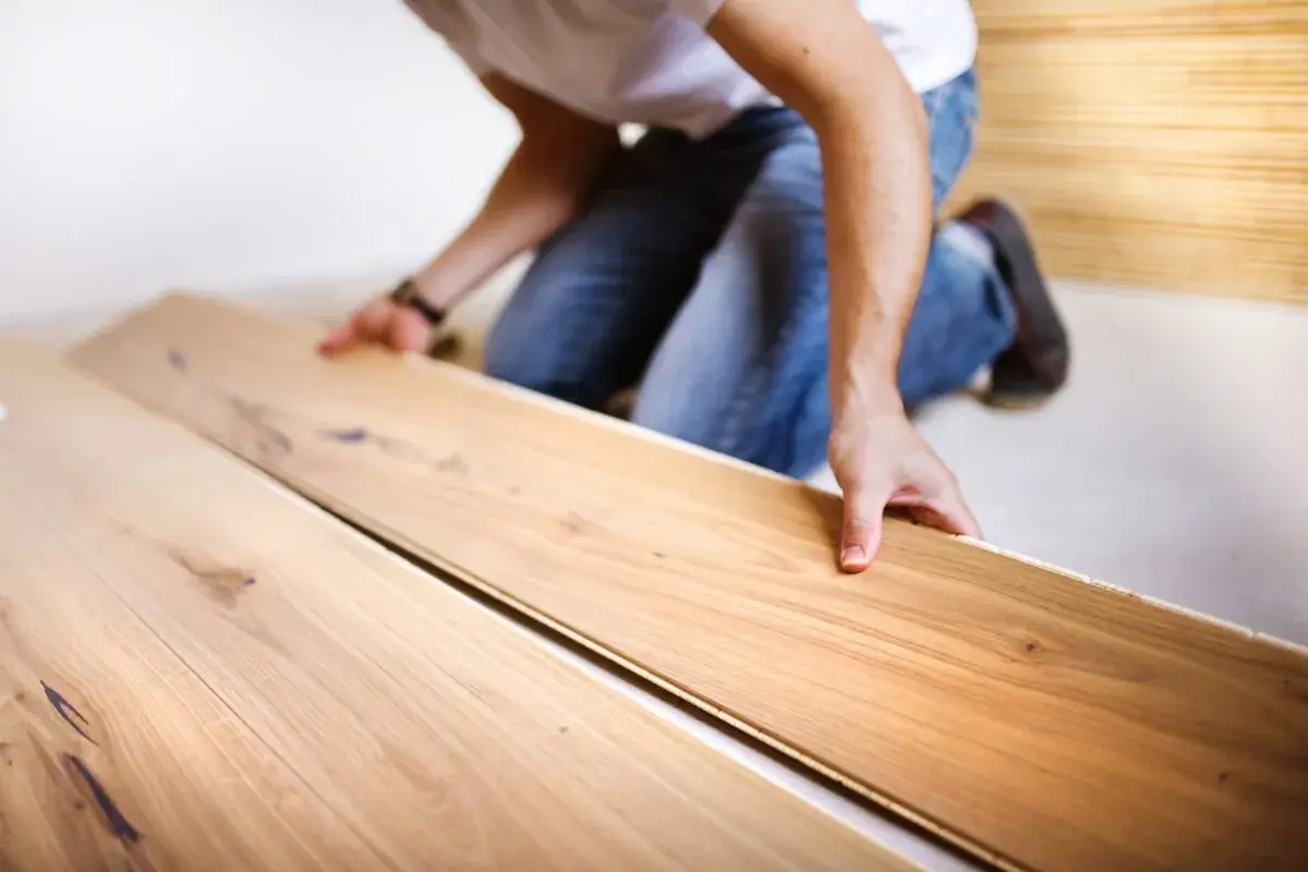 Uomo in ginocchio posa assi di legno per un pavimento con schema a spina di pesce.