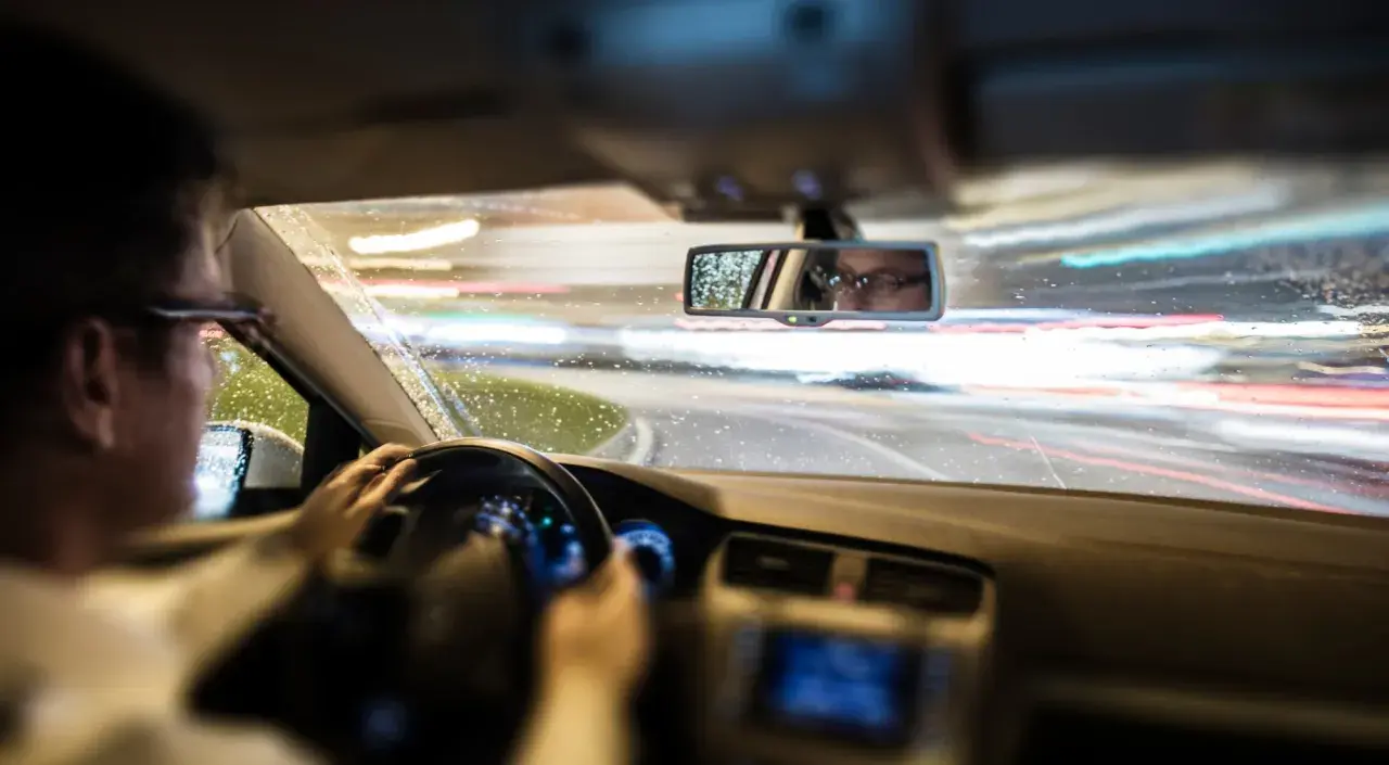Conductor con gafas al volante de noche, con lluvia y luces de coches borrosas. El ASR de un coche ayuda a mantener la tracción en estas condiciones.