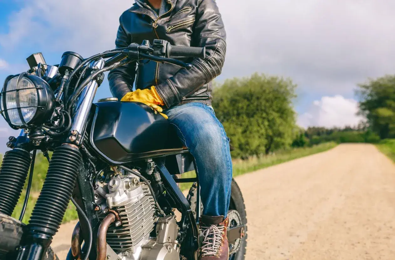 Motociclista con chaqueta de cuero y guantes amarillos, listo para la aventura. ¿Dyneema vs Kevlar? ¡La carretera espera!