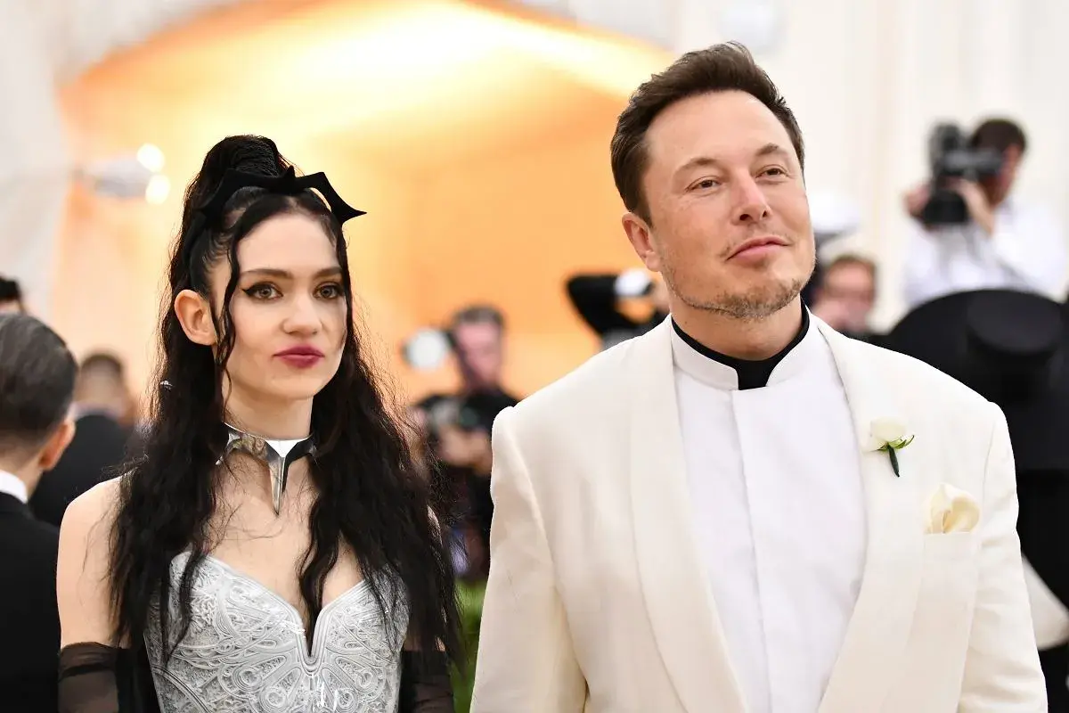Grimes i Elon Musk na czerwonym dywanie. Ona w srebrnej kreacji z nietypowym naszyjnikiem, on w białej marynarce.