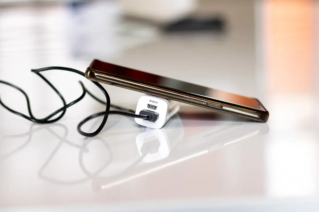 Smartfon podłączony do ładowarki, by zapobiec nadmiernemu zużyciu baterii.