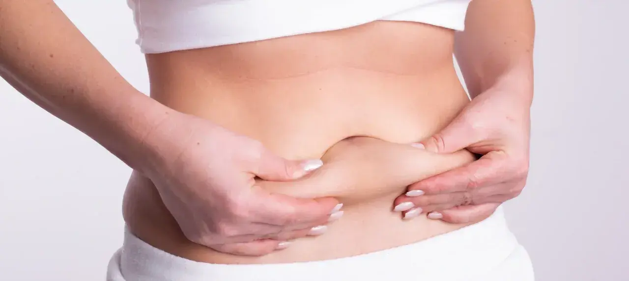 Manos pellizcando la piel del abdomen, mostrando la distensión abdominal por ansiedad.