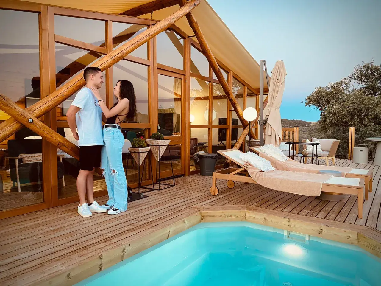 Pareja disfrutando de la tranquilidad de la dehesa experiences, con piscina y tumbonas en una cabaña de madera.