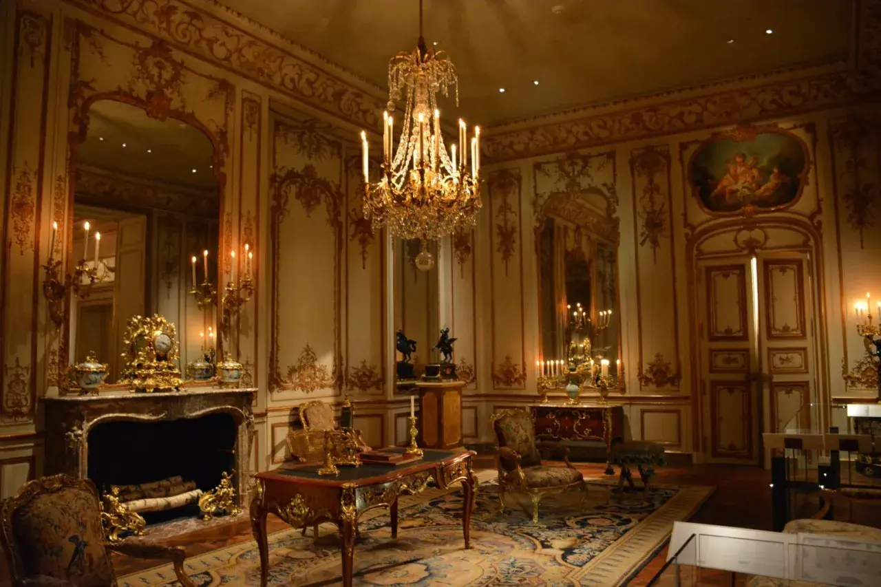 A lavish room with a crystal chandelier, ornate gold trim, and antique furniture embodies the royalcore aesthetic.