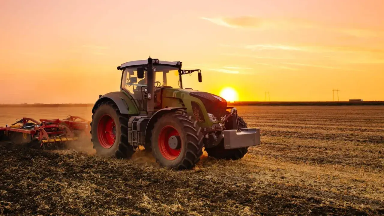Un tracteur, c'est ce puissant engin vert et rouge qui travaille la terre au coucher du soleil, préparant le champ pour les futures récoltes.