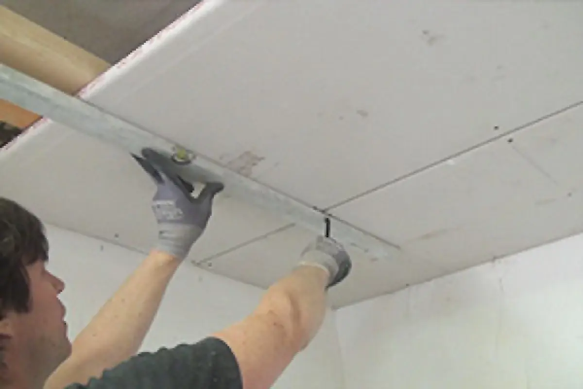 Handwerker bearbeitet Decke mit Rigipsplatten. Die Dicke der Platten ist entscheidend für Stabilität und Dämmung.
