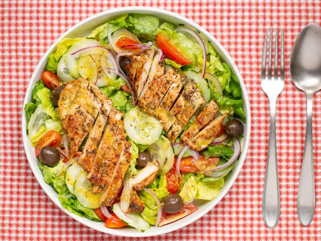 Deliciosa ensalada de pollo a la parrilla con lechuga, tomate, pepino, cebolla morada y aceitunas.