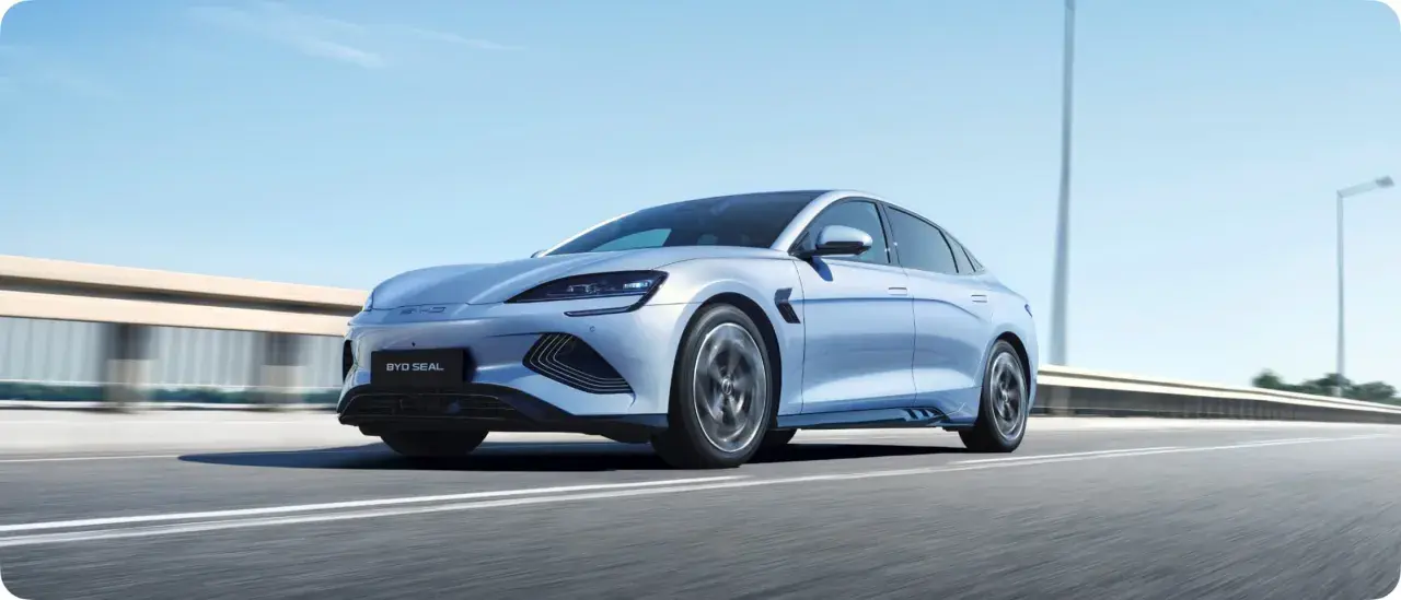 Un elegante veicolo elettrico BYD Seal sfreccia su un'autostrada soleggiata, con il cielo azzurro e le luci stradali sfocate sullo sfondo.