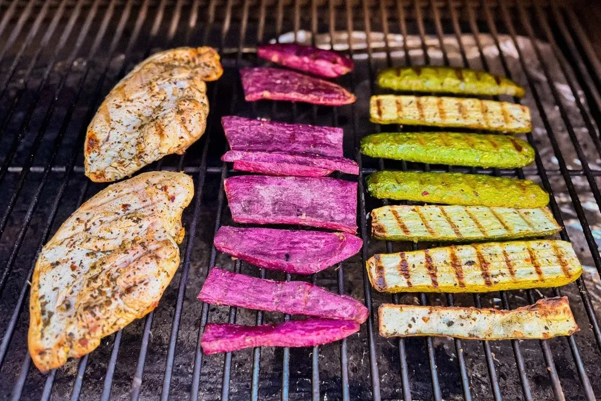 Deux blancs de poulet au barbecue, accompagnés de tranches de patate douce violette et de courgettes grillées, sur une grille.