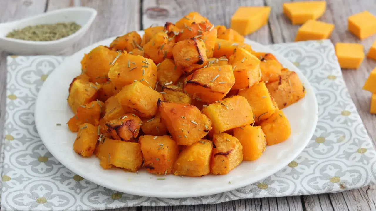 Zucca in friggitrice ad aria, dorata e profumata, servita su un piatto bianco con erbe aromatiche.