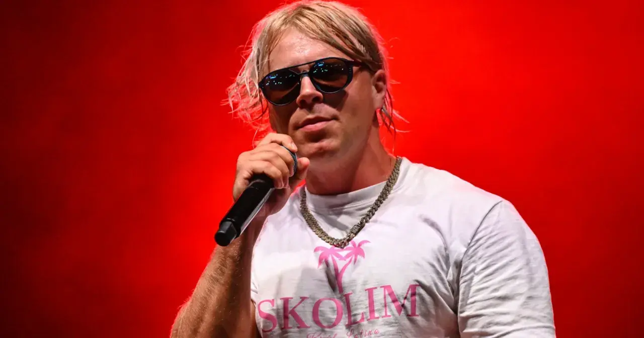 Artysta Skolim w okularach i białej koszulce z napisem "SKOLIM" na czerwonym tle. Zastanawiasz się, ile Skolim bierze za koncert?