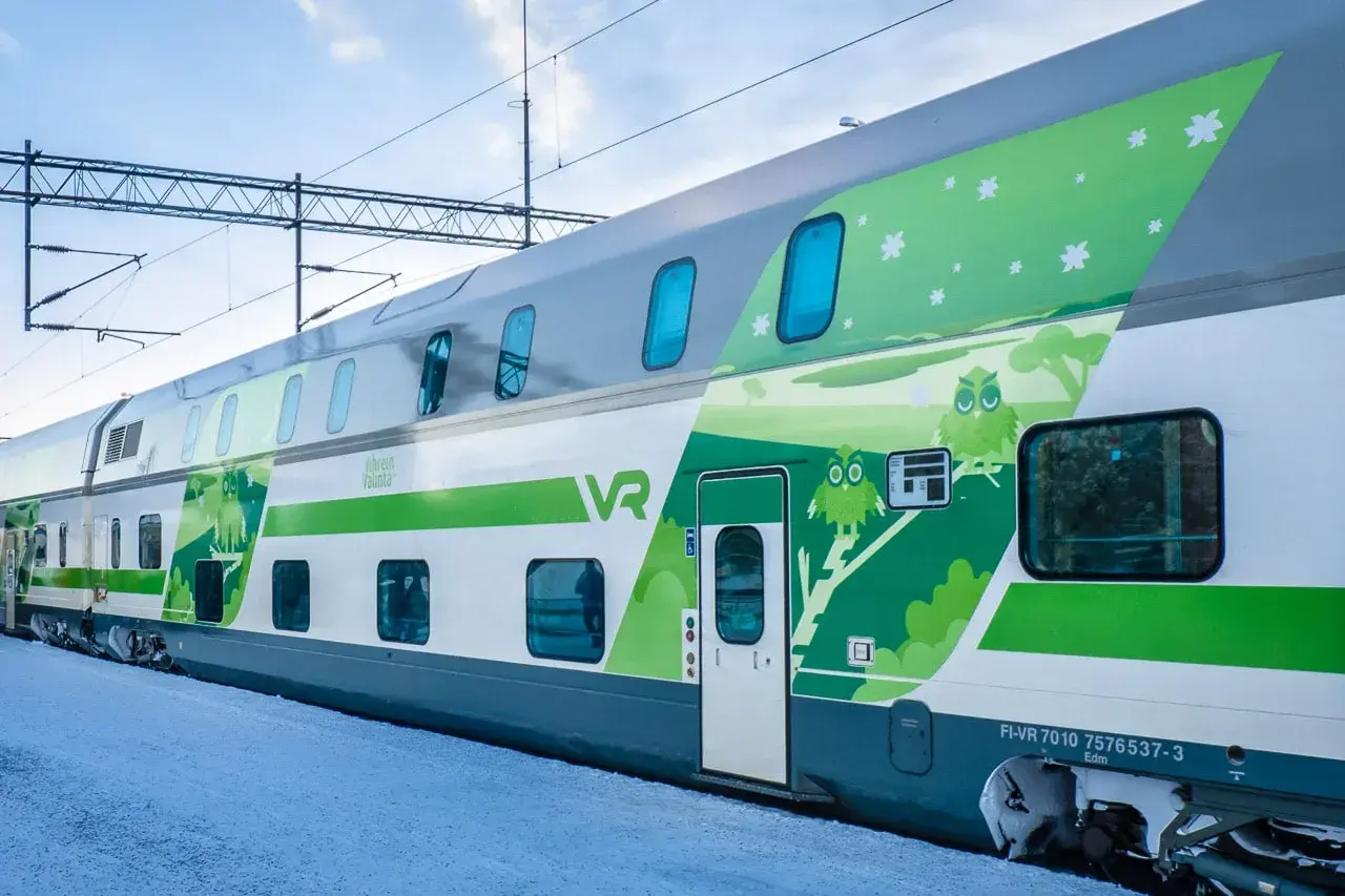 Ein moderner Doppelstockzug der VR in Finnland, verziert mit Eulen und Sternen, fährt durch eine verschneite Landschaft.
