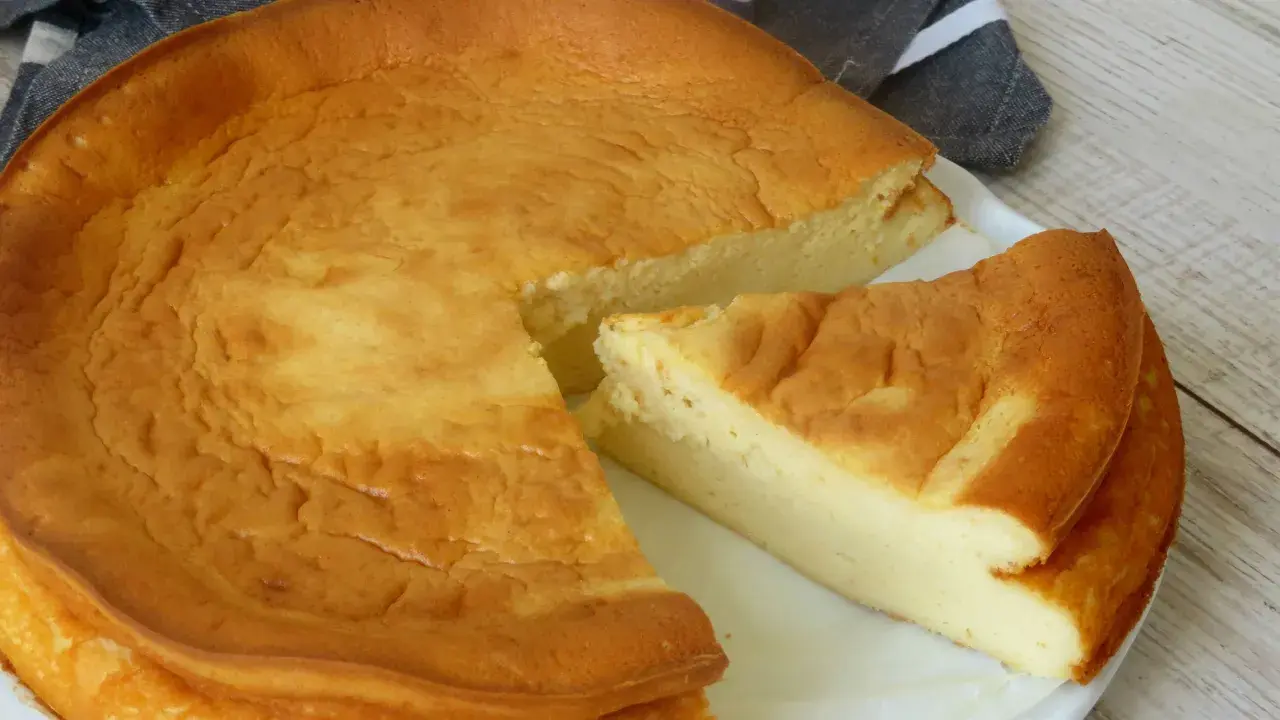 Tarta de queso Philadelphia dorada y esponjosa, con una porción cortada que revela su interior cremoso.