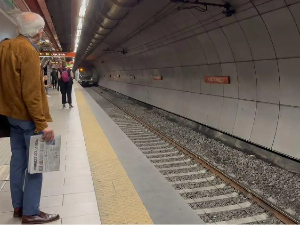 Uomo attende treno alla stazione Valle Aurelia Termini, con giornale in mano.