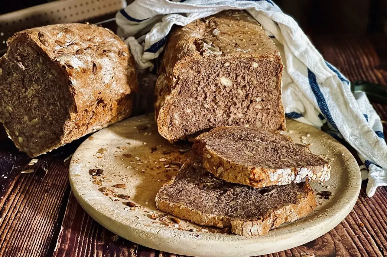 Frisch gebackenes Dinkelbrot mit Körnern und Nüssen, auf einem Holzbrett mit zwei Scheiben.