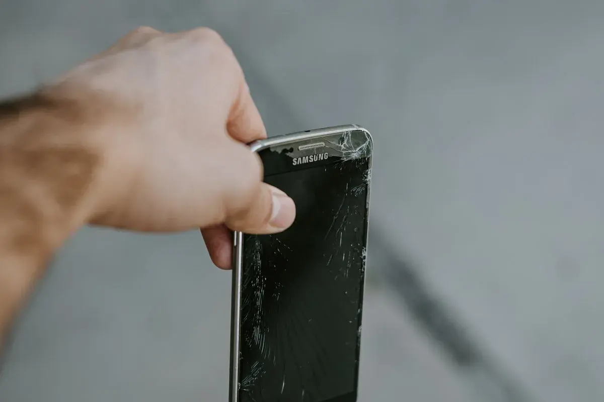 En hand håller en trasig Samsung-mobil. Dags att återvinna mobiltelefonen för att spara på jordens resurser.