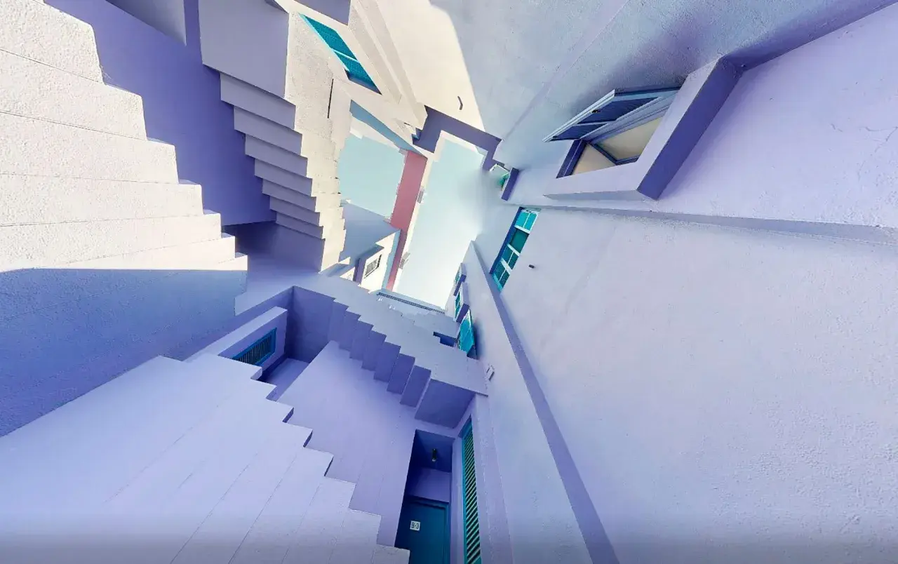 Escaleras y fachadas de color lavanda y blanco, con toques turquesa, que recuerdan a la muralla roja de Calpe.