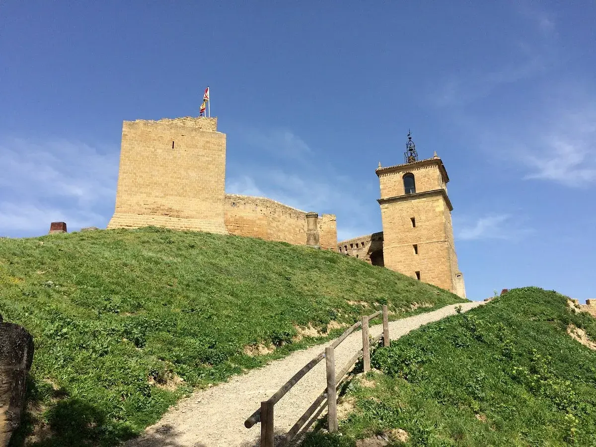 El castillo de San Vicente de la Barquera se alza majestuoso sobre una colina verde, con su torre y murallas de piedra bajo un cielo azul.