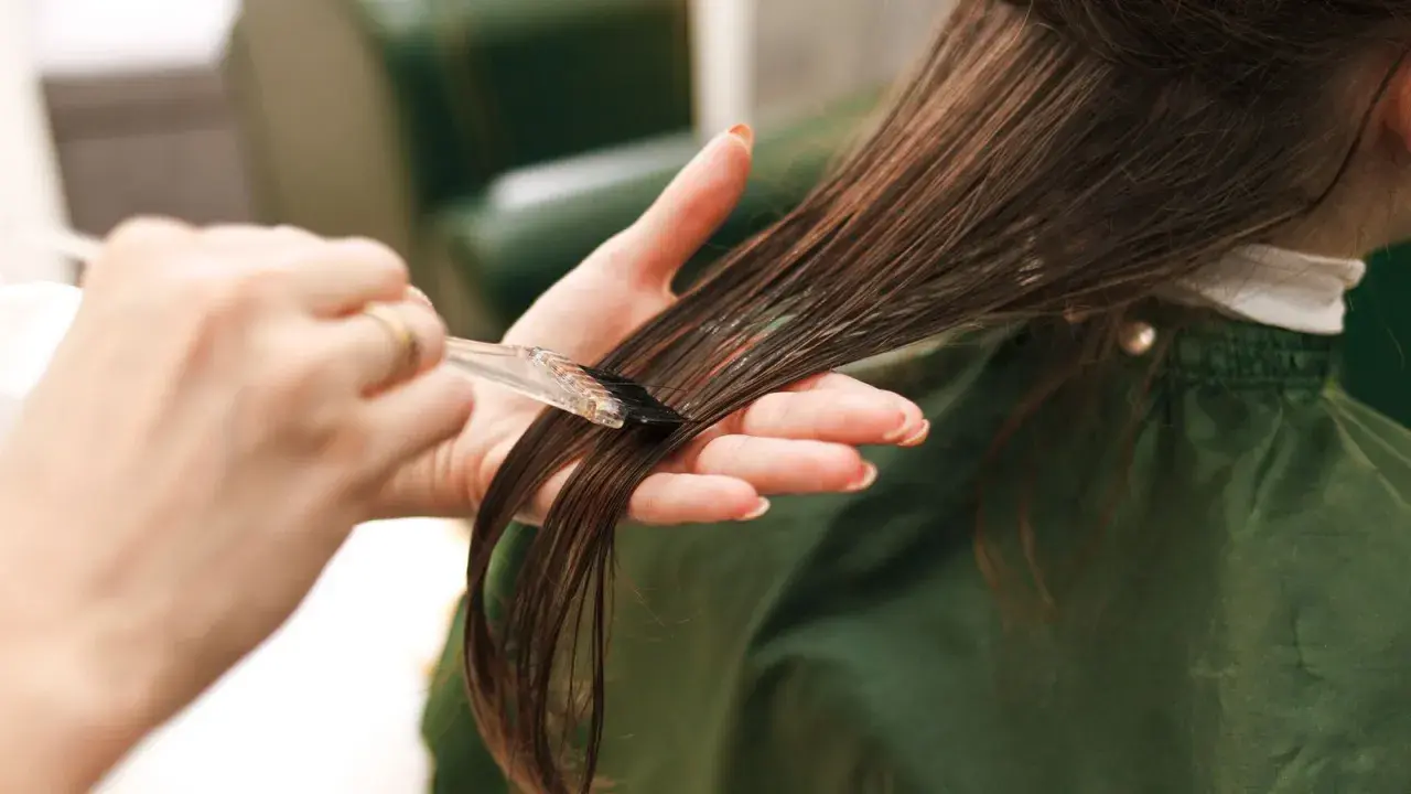 Manos aplicando tinte en el cabello. Cuidado con la alergia al tinte de pelo.