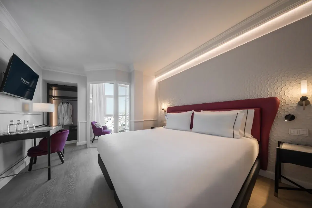 Habitación moderna y luminosa en el hotel San Antón Granada. Cama doble con cabecero rojo, escritorio, sillón morado y vistas.