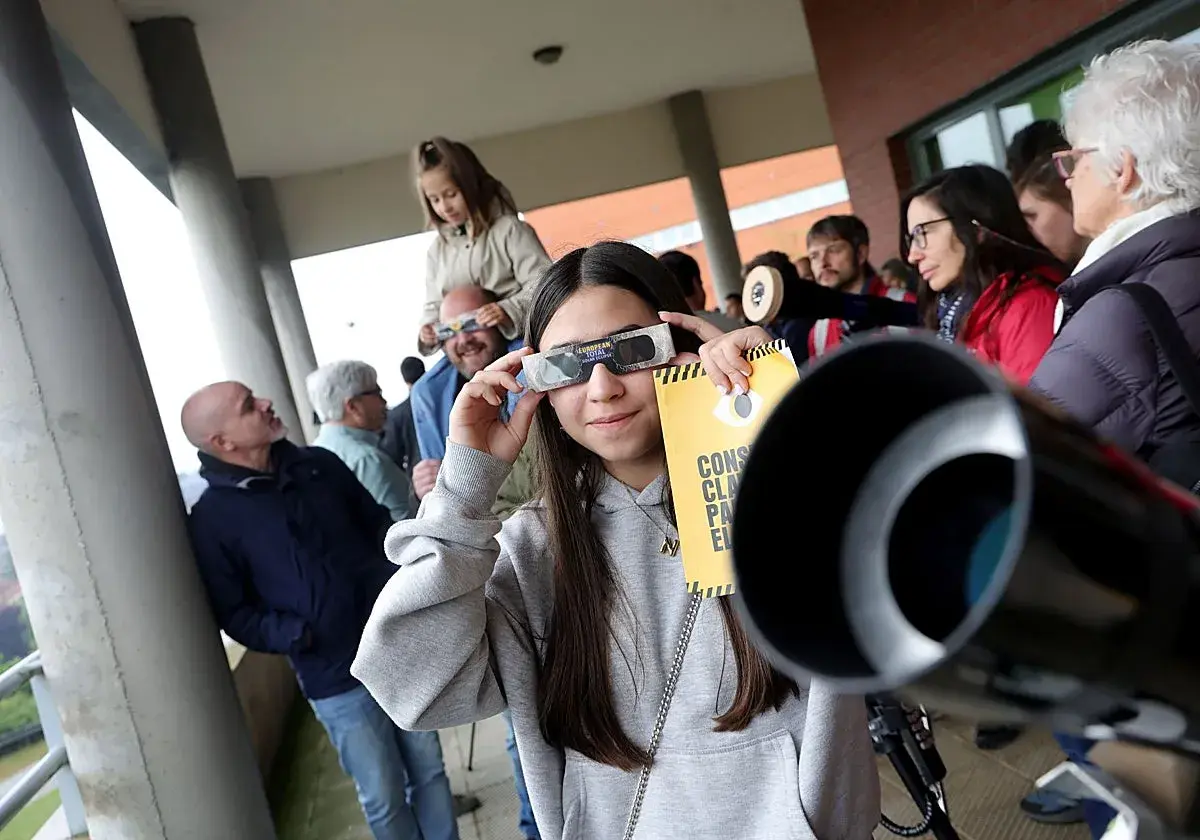 Joven mira un eclipse con gafas especiales, cerca de un telescopio con forma de lámpara cónica.