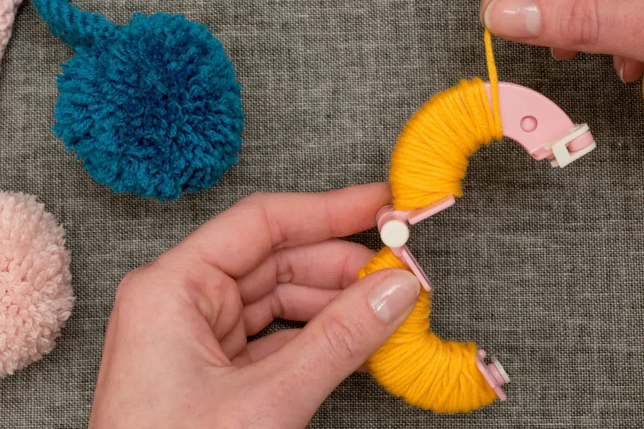 Hände wickeln gelbes Garn um eine Pompon-Schablone. Tolle Pompon-Ideen für dein nächstes Projekt!