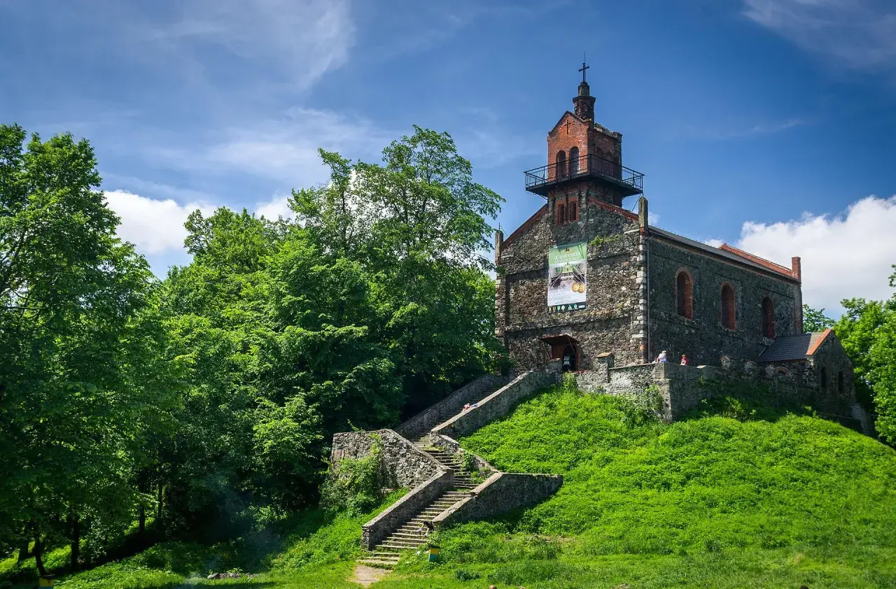 Kamienny kościół na wzgórzu, z kamiennymi schodami prowadzącymi do wejścia. Wokół bujna zieleń, idealne miejsce na odkrywanie dzierżoniów atrakcje.