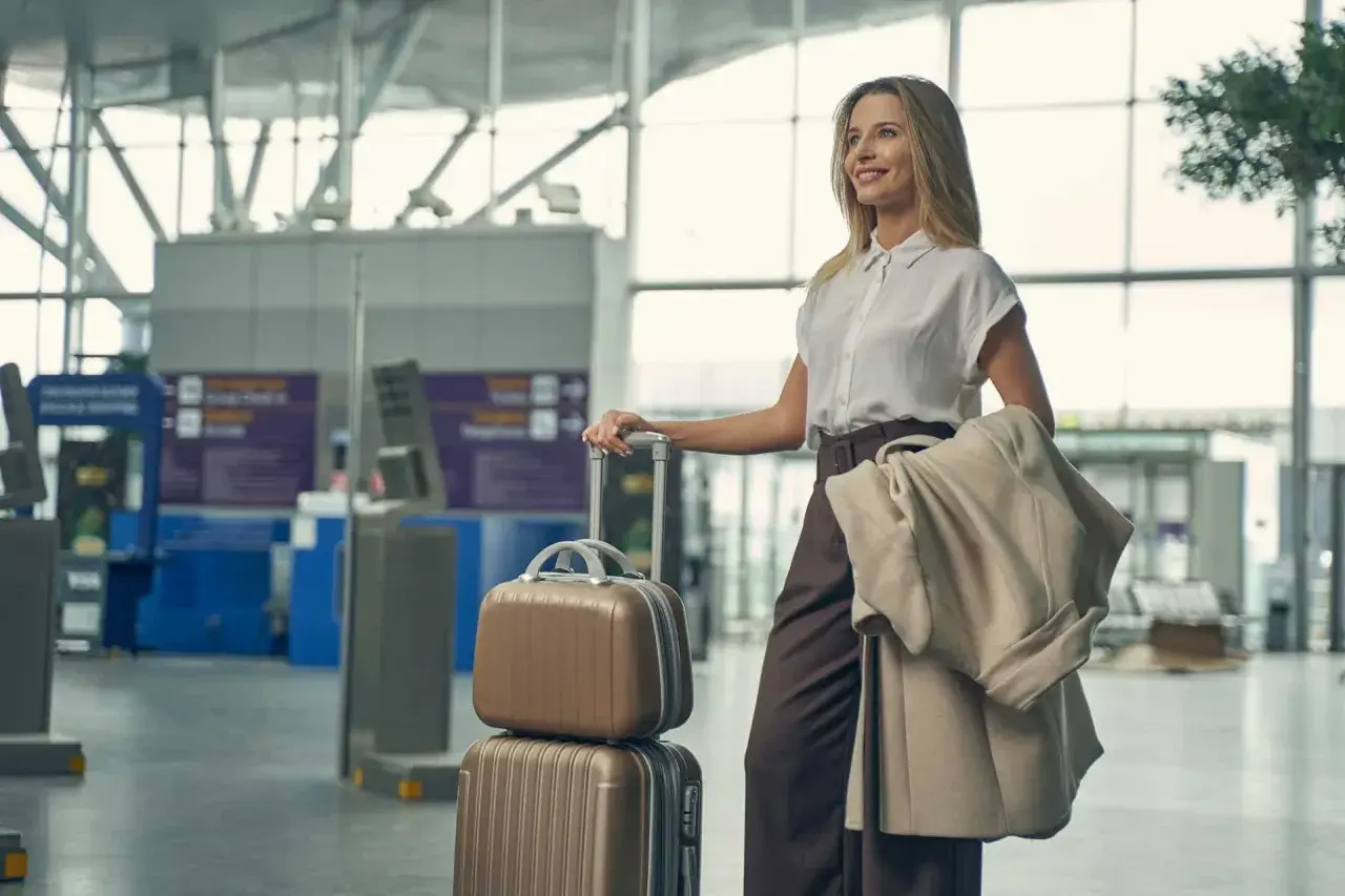 Elegancka kobieta w stylowym ubraniu do samolotu, z walizkami i płaszczem, czeka na lotnisku.