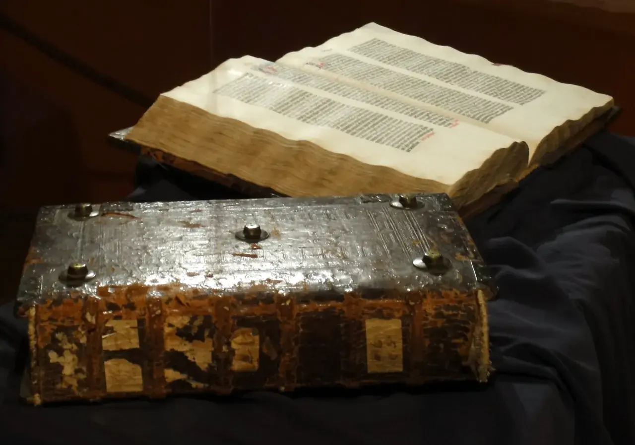 Stary, zniszczony księgozbiór w stylu biblijnym, z metalowymi okuciami i otwartą księgą pełną tekstu.