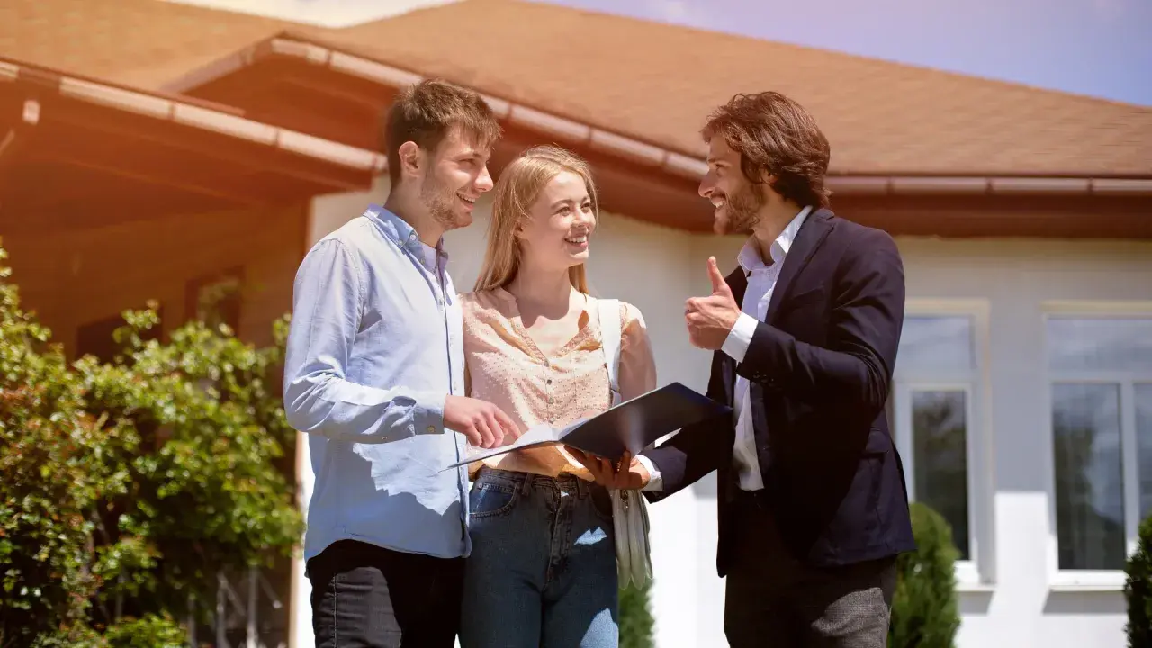 Un couple discute avec un agent immobilier devant une maison, signe d'une vente en cascade réussie.