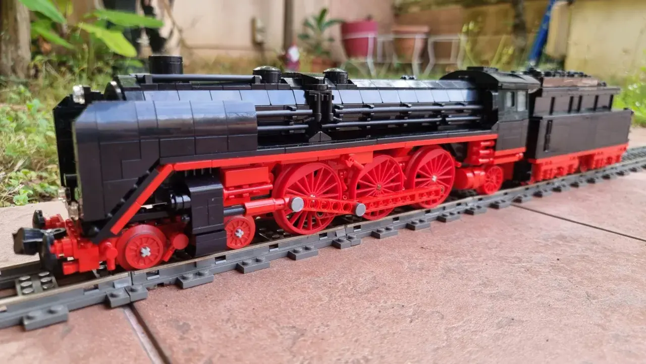 Detailreiche Lego Dampflok MOC mit roten Rädern und schwarzem Gehäuse auf Schienen.