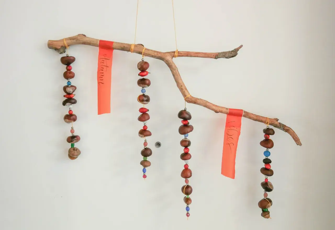 Ein schönes Herbst-Mobile zum Basteln mit Kindern: Kastanien, Beeren und bunte Perlen hängen an einem Ast.