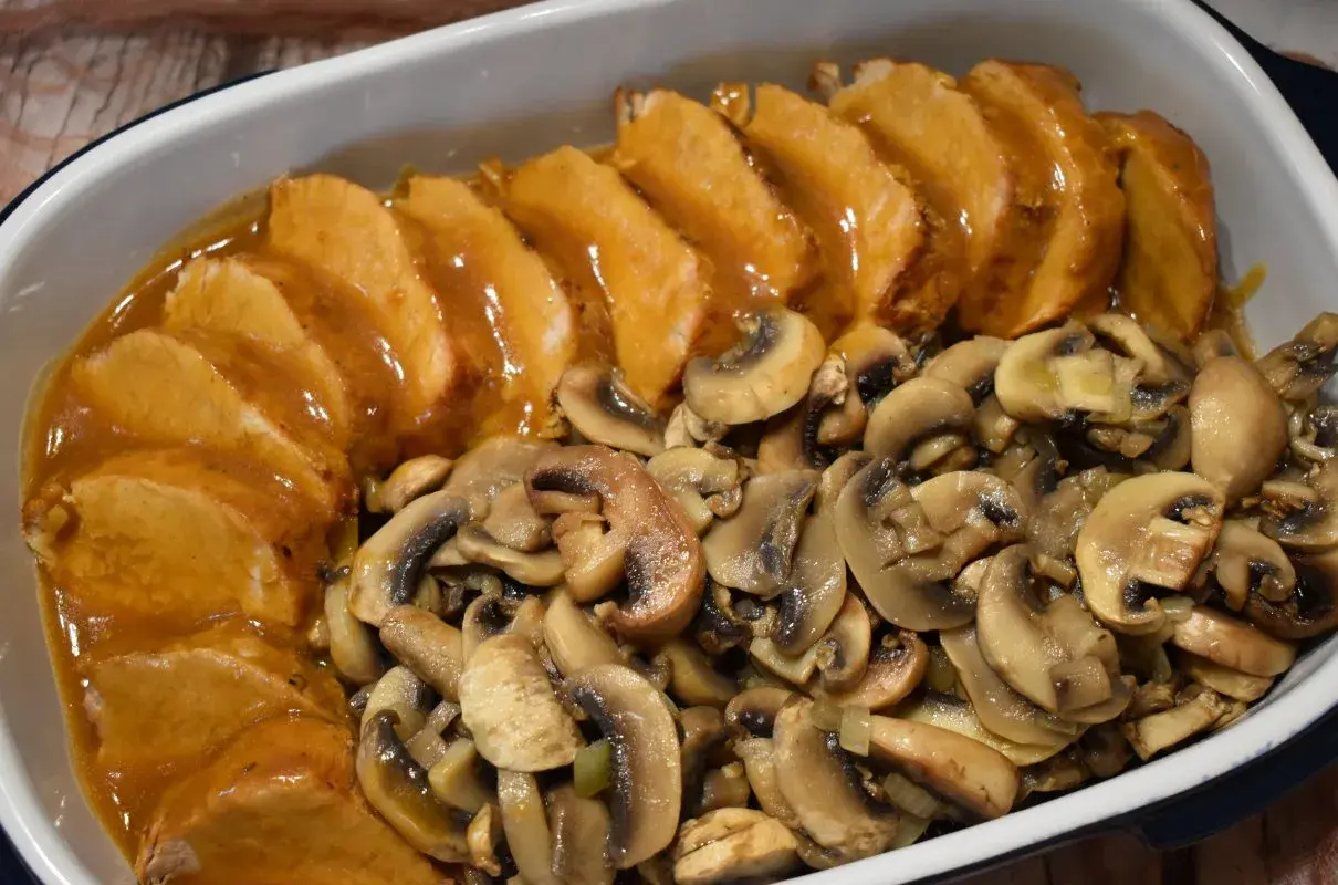 Pyszny schab z pieczarkami w sosie, podany w naczyniu żaroodpornym. Aromatyczne pieczarki idealnie komponują się z soczystym mięsem.