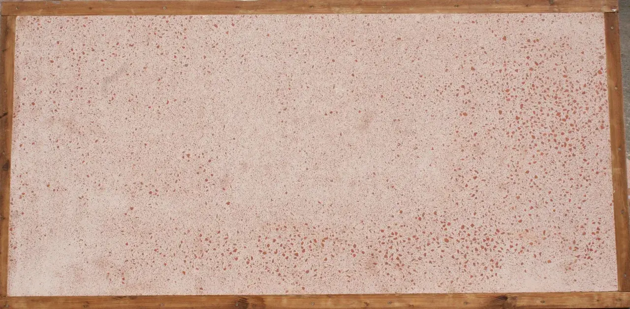 Superficie in coccio pesto con venature rosse, incorniciata da listelli di legno grezzo.